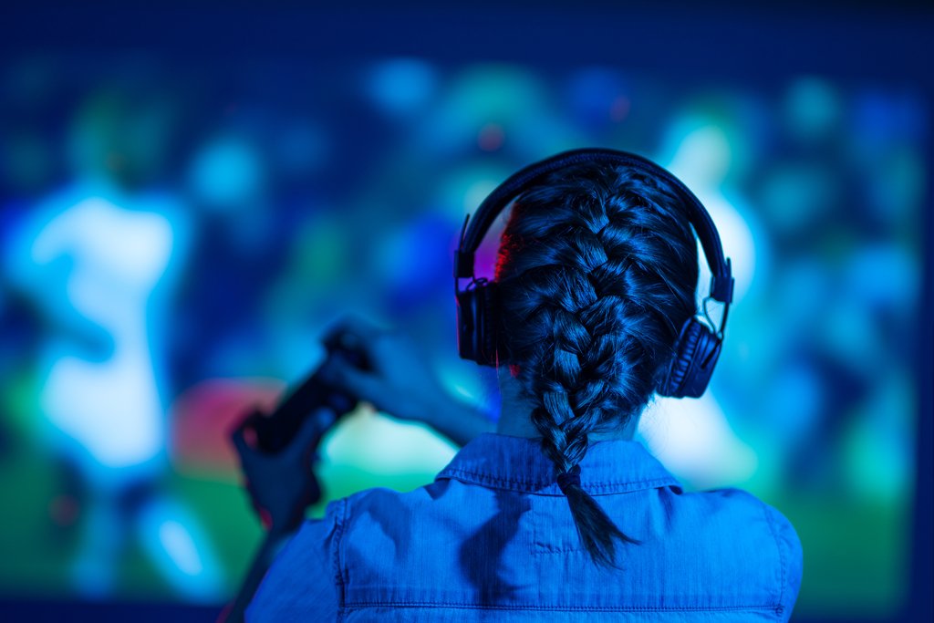 A person with braided hair wears headphones and holds a game controller, focused on a colorful screen.